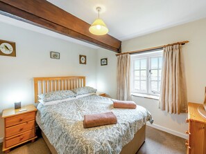 A bedroom with a wooden headboard, a bed with patterned bedding, a bedside table with a lamp, and a window with curtains. - Granary Cottage - E5634 (Chittlehampton, near Umberleigh)