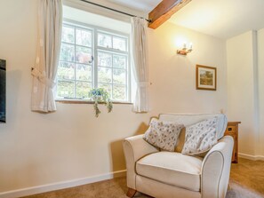 A cozy room with a beige sofa, a window with curtains, a wall-mounted light fixture, and a framed picture. - Granary Cottage - E5634 (Chittlehampton, near Umberleigh)