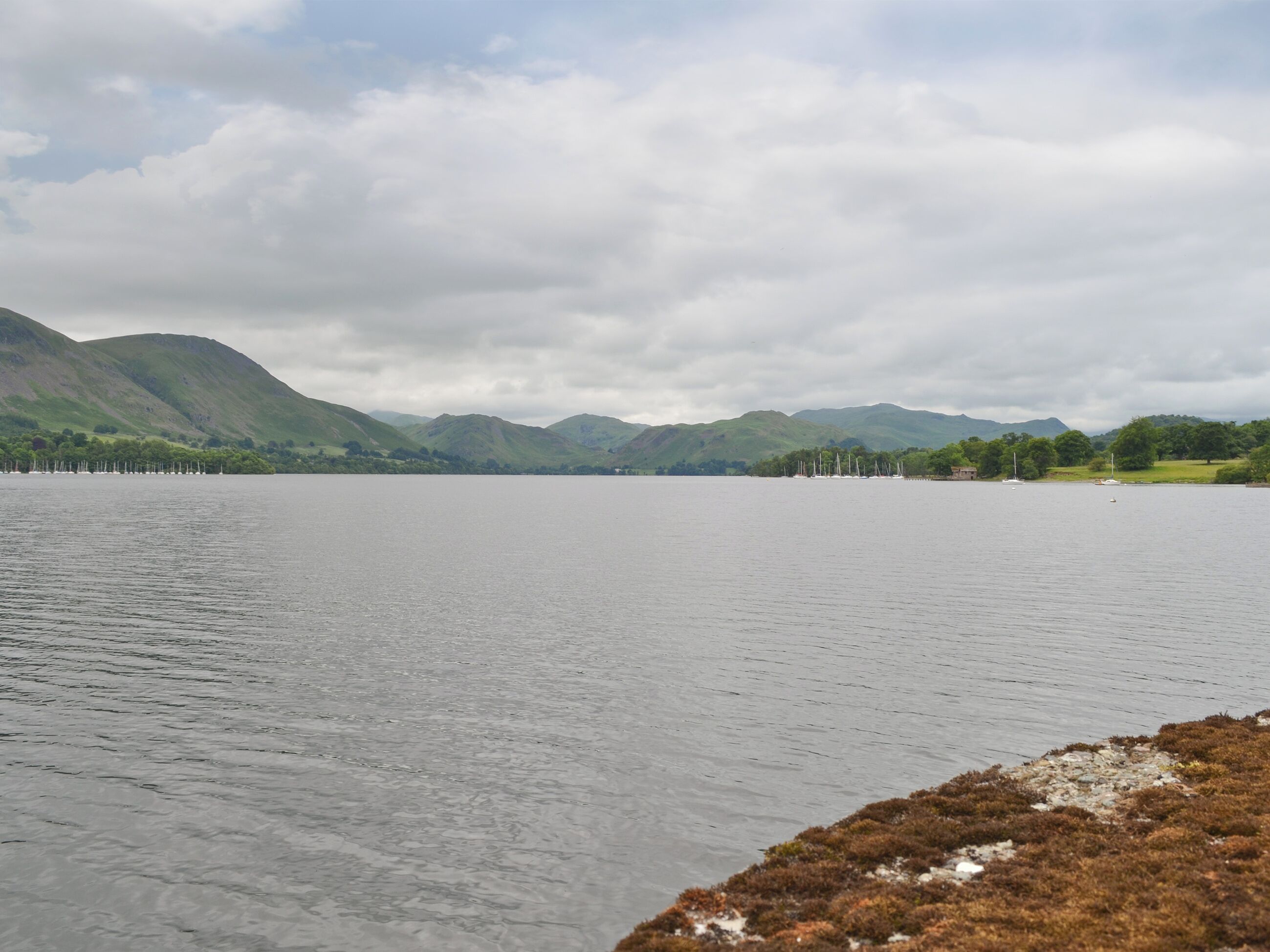 A lake with mountains in the background and a grassy area with boats.