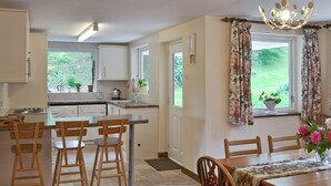 Una cocina con comedor, sillas de madera, una mesa con mantel floreado y una araña.