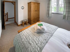 A bedroom with a bed, a wooden wardrobe, a small stool, and a window with curtains. - 3 bedroom accommodation in Treffynnon, near St Davids (Treffynnon, near St Davids)