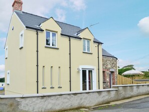 A two-story house with a yellow facade, a stone tower, and a white door. - 3 bedroom accommodation in Treffynnon, near St Davids (Treffynnon, near St Davids)