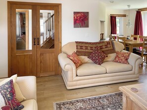 A living room with a beige sofa, patterned throw, and a wooden door. - 3 bedroom accommodation in Treffynnon, near St Davids (Treffynnon, near St Davids)