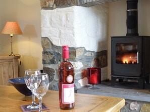 A wooden table with a wine bottle, two glasses, and a candle. A stone wall and a fireplace with a log fire are in the background. - 3 bedroom accommodation in Treffynnon, near St Davids (Treffynnon, near St Davids)