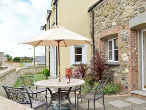 Een ronde tafel met een beige parasol, omringd door metalen stoelen, geplaatst tegen een stenen muur met een raam.