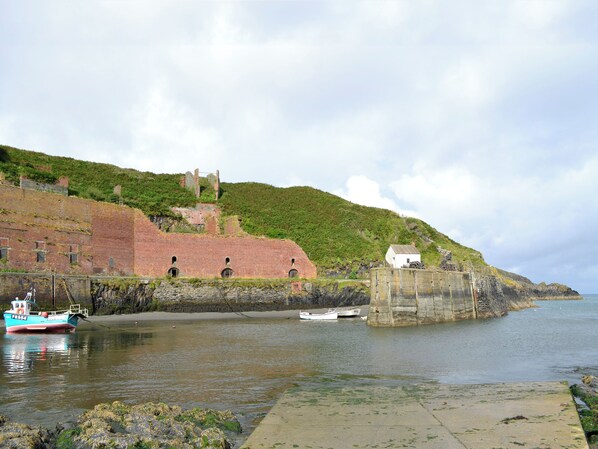A coastal scene with a brick wall, a small white building, and a rocky outcrop.
