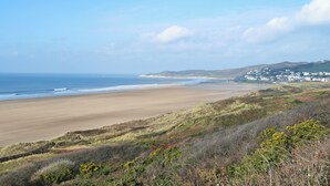 Paisagem costeira com uma praia arenosa, colinas suaves e um povoado ao longe.