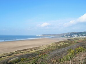 A coastal landscape with a sandy beach, rolling hills, and a distant settlement. - 1 bedroom accommodation in Ilfracombe (Ilfracombe)