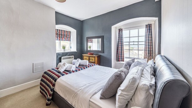 Quarto com cama, mesa de cabeceira, espelho, janela com cortinas e luminária vermelha.