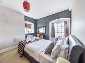 Un dormitorio con cama, mesita de noche, espejo, ventana con cortinas y una lámpara roja.