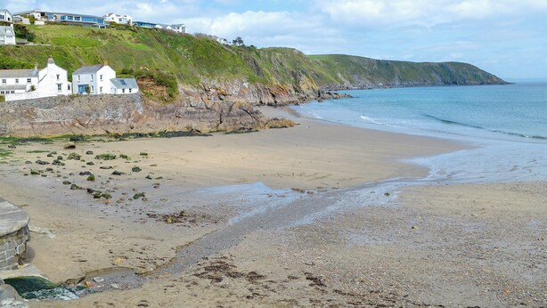 Une plage côtière avec des maisons construites sur une falaise, un rivage sablonneux et une mer calme.