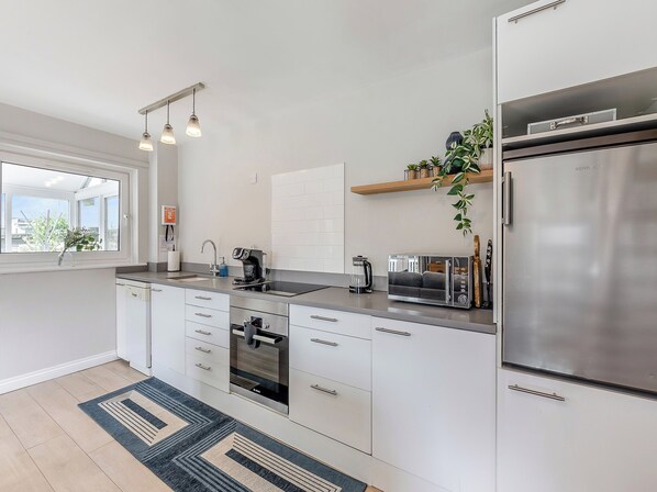A modern kitchen with white cabinets, a stainless steel refrigerator, a coffee maker, and a toaster. - Water's Edge Holiday Home (Beadnell)