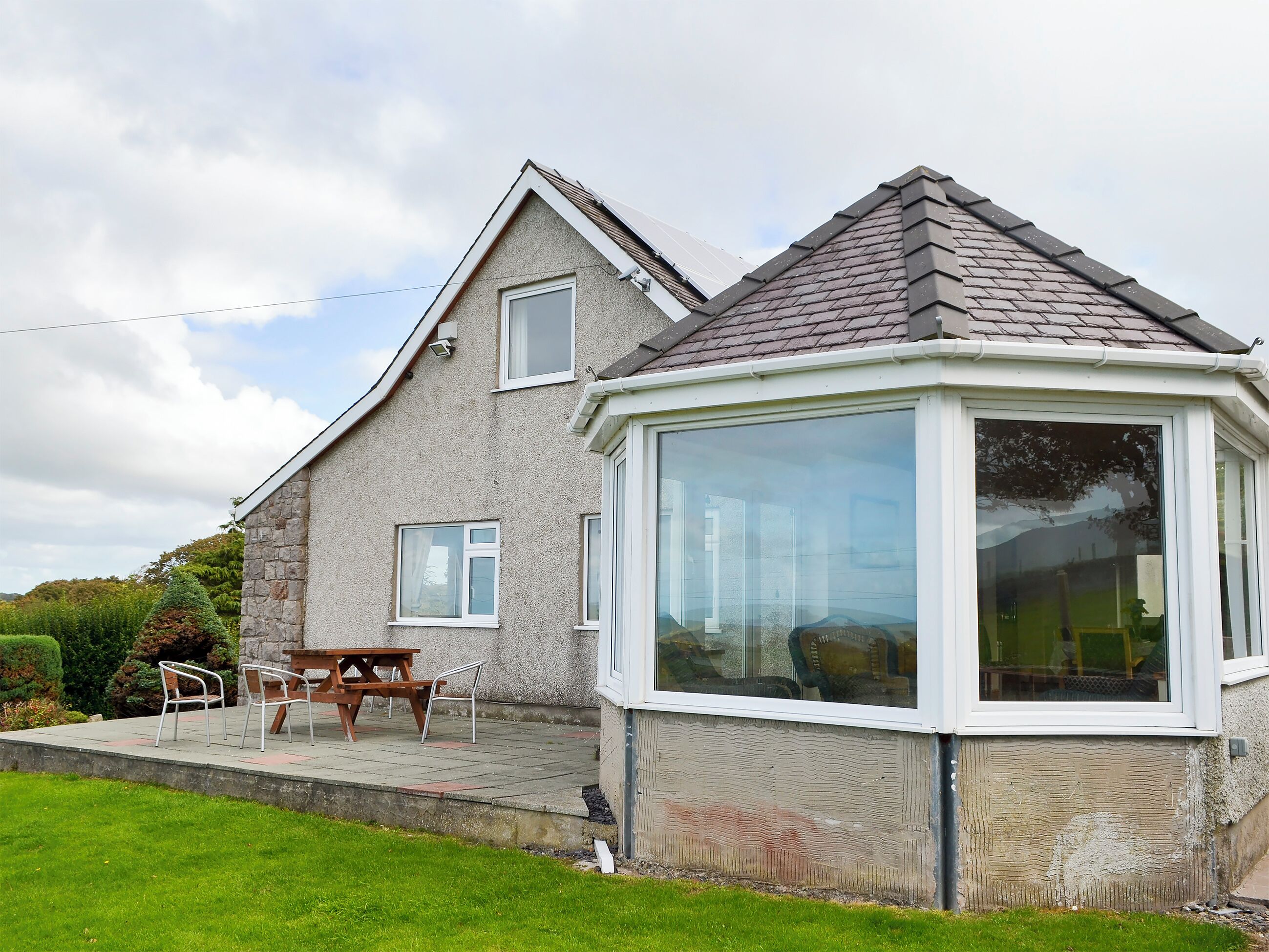 A house with a large bay window, a stone exterior, and a patio with outdoor furniture.