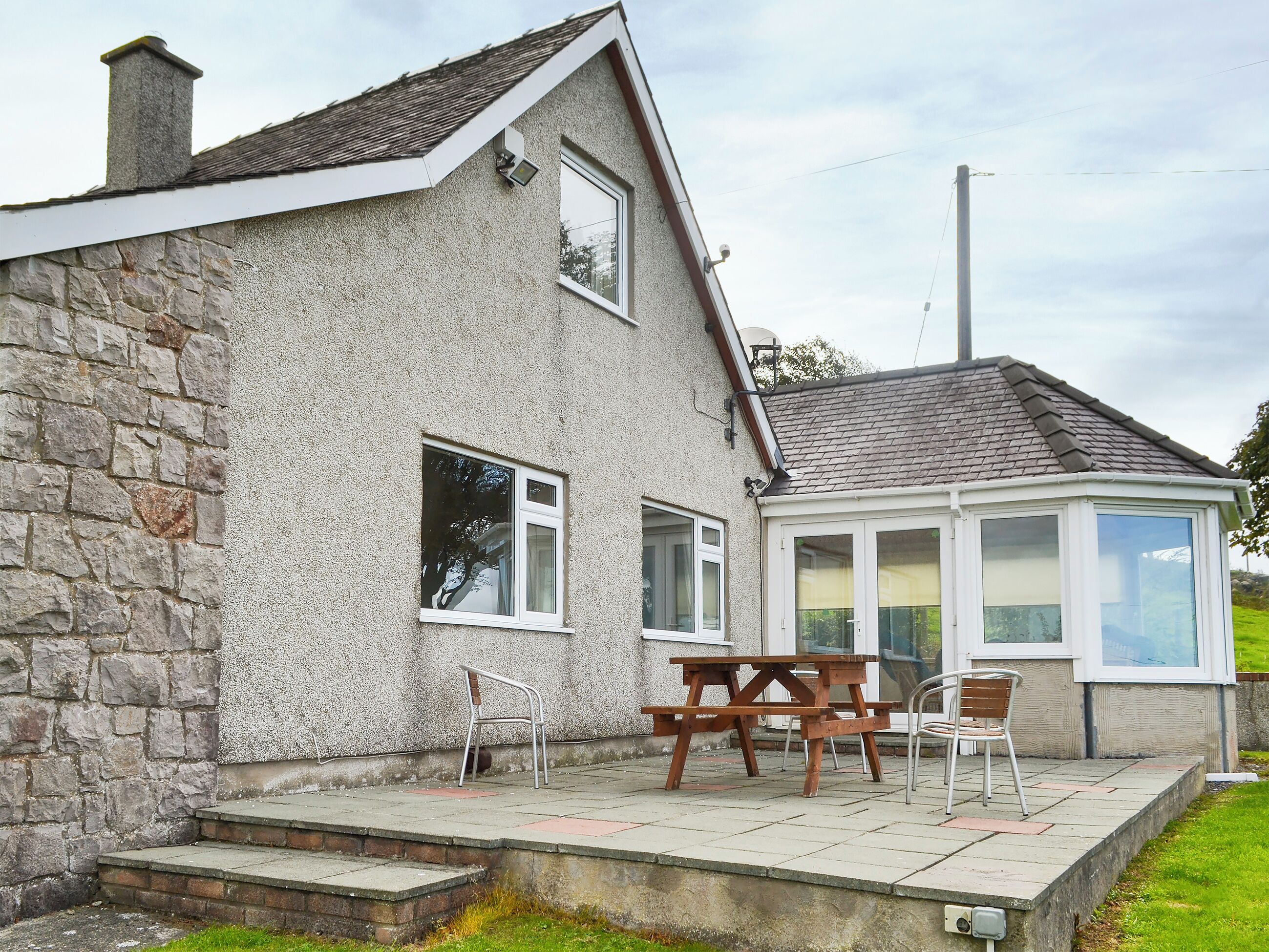 A stone house with a covered patio, a wooden table, and two chairs.