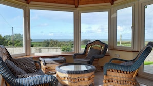 A sunroom with wicker furniture, large windows, and a view of the sea.