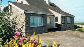 A stone house with a sloped roof, large windows, and a driveway leading to the entrance.