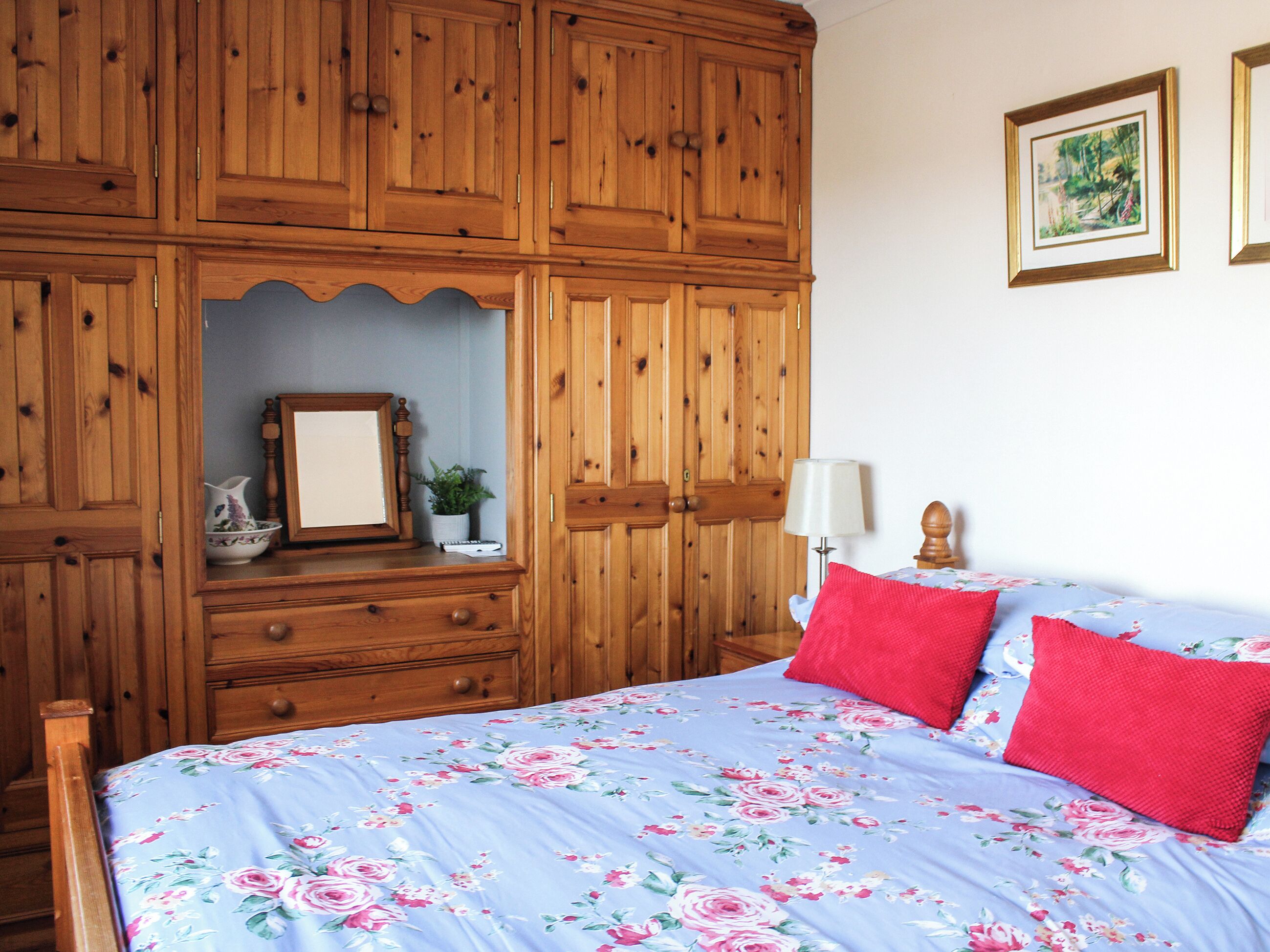 Une chambre avec une armoire en bois, un lit avec une literie à motifs floraux et une table de chevet avec une lampe.