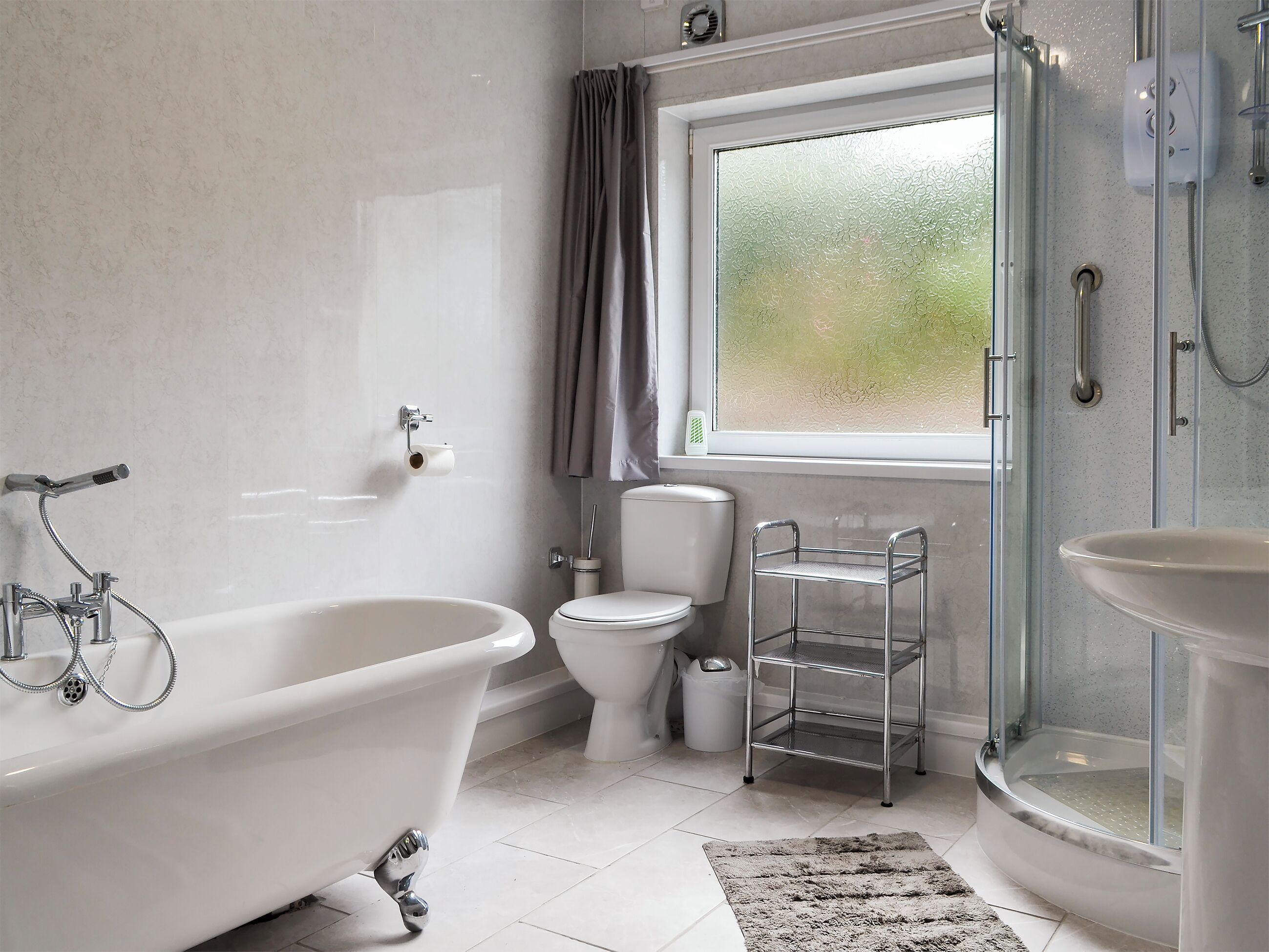 A bathroom with a bathtub, toilet, shower, and a window with curtains.