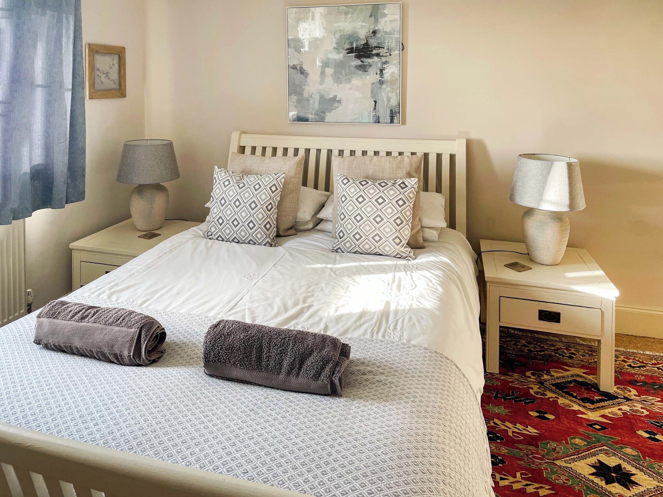 A neatly made bed with patterned pillows, a bedside lamp, and a rug.