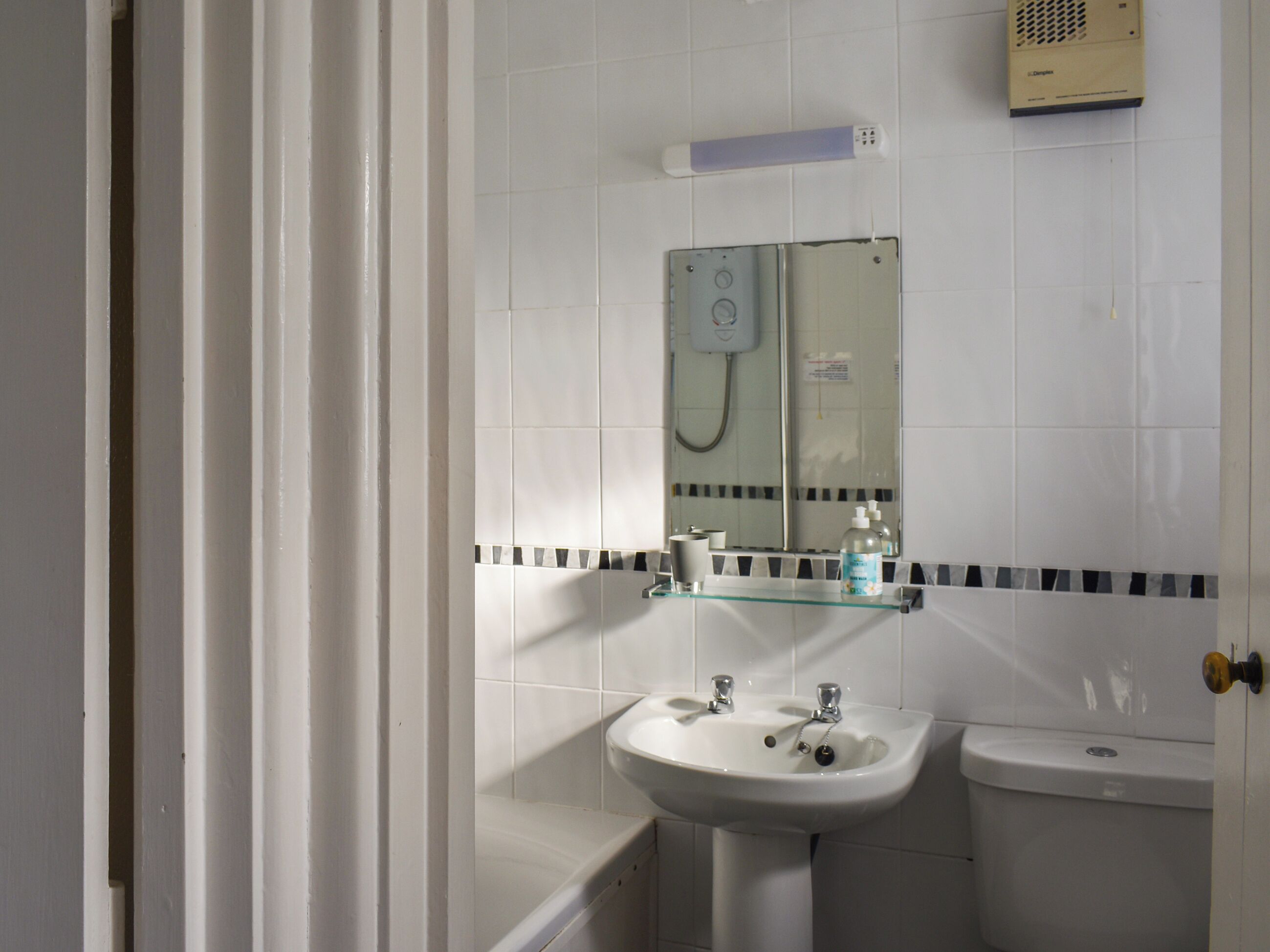 Une salle de bain avec un lavabo blanc, un miroir, une étagère en verre et des toilettes.