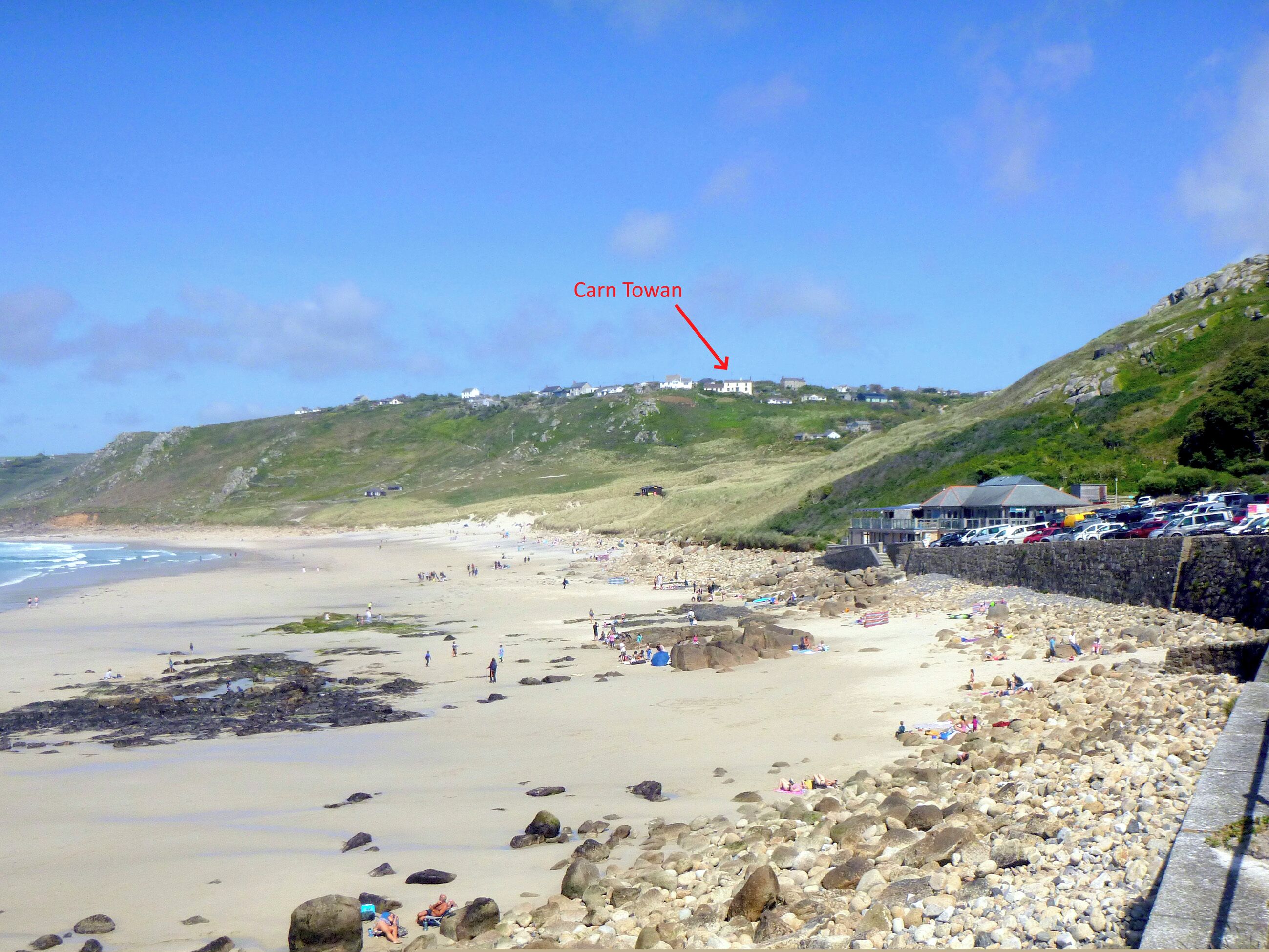 A beach with rocky areas, a parking lot, and a building labeled "Carn Towan" on a hill.