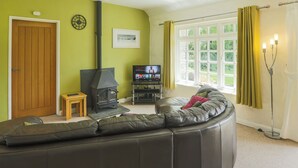 A living room with a sofa, a small wooden table, a fireplace, a television, and a window with curtains. - 3 bedroom accommodation in Advent (Advent)