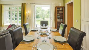 A dining room with a wooden table set for four, surrounded by leather chairs, with a view of greenery outside. - 3 bedroom accommodation in Advent (Advent)