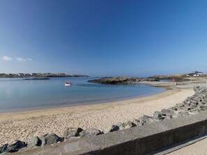 A coastal beach with a clear sky, calm water, and a rocky shoreline.