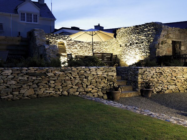 A stone wall with a wooden bench and a table under a large umbrella.