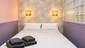 A hotel room with a patterned wallpaper, two wall-mounted light fixtures, a bed with a textured bedspread, and two folded towels on the floor. - POOL TERRACE APARTMENT TOSSA DE MAR (Tossa de Mar)
