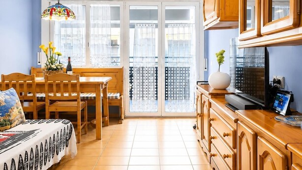 A room with a dining table, chairs, a sofa, a TV, wooden cabinets, and a large window with a view. - POOL TERRACE APARTMENT TOSSA DE MAR (Tossa de Mar)
