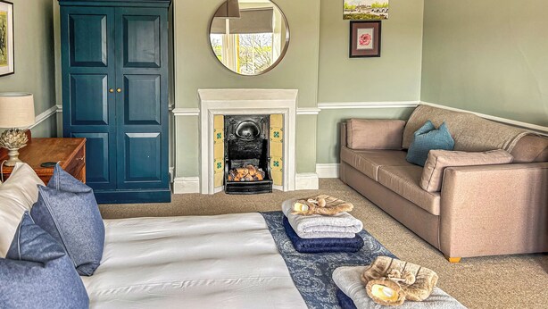 A room with a bed, a sofa, a fireplace, a cabinet, and a mirror. - 4 bedroom accommodation in Christon Bank, near Embleton (Christon Bank, near Embleton)