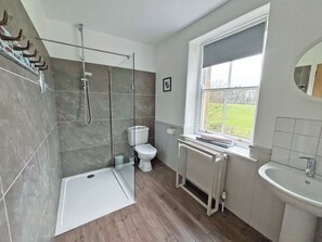 Un baño con ducha, inodoro, radiador y ventana con vistas.