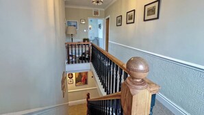 A staircase with a wooden handrail and black balusters, leading to a landing with a lamp and framed pictures. - 4 bedroom accommodation in Christon Bank, near Embleton (Christon Bank, near Embleton)