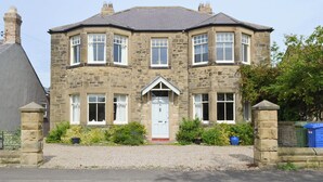 A stone-built house with a central entrance, multiple windows, and a gravel driveway. - 4 bedroom accommodation in Christon Bank, near Embleton (Christon Bank, near Embleton)