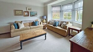 A living room with two sofas, a coffee table, and a lamp. There are framed pictures on the wall and large windows with a view outside. - 4 bedroom accommodation in Christon Bank, near Embleton (Christon Bank, near Embleton)