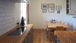 A kitchen with a wooden countertop, a sink, cabinets, a dining table with chairs, and wall-mounted artwork. - 4 bedroom accommodation in Christon Bank, near Embleton (Christon Bank, near Embleton)