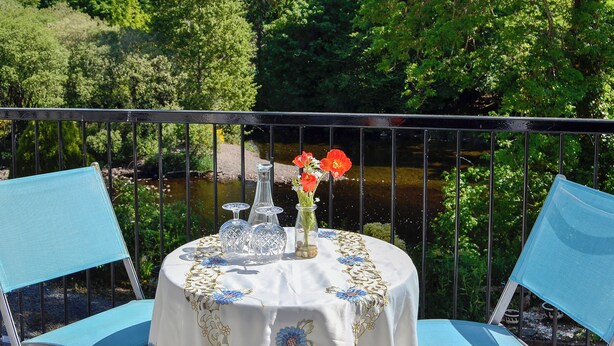 Ein Tisch gedeckt mit einer weißen Tischdecke und blauen Stühlen, mit Blick auf einen Fluss und Bäume im Hintergrund.