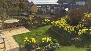 A patio area with a table and chairs, surrounded by a wooden fence and a garden with yellow flowers. - 2 bedroom accommodation in Staithes, Cleveland (Staithes, Cleveland)