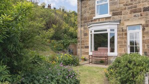A stone house with a bay window, a garden with various plants and flowers, and a bench. - 2 bedroom accommodation in Staithes, Cleveland (Staithes, Cleveland)