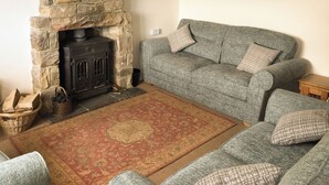 A cozy living room with a stone fireplace, a grey sofa, and a patterned rug. - 2 bedroom accommodation in Staithes, Cleveland (Staithes, Cleveland)
