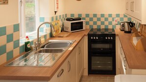 A compact kitchen with a sink, microwave, stove, and a clock on the wall. - 2 bedroom accommodation in Staithes, Cleveland (Staithes, Cleveland)