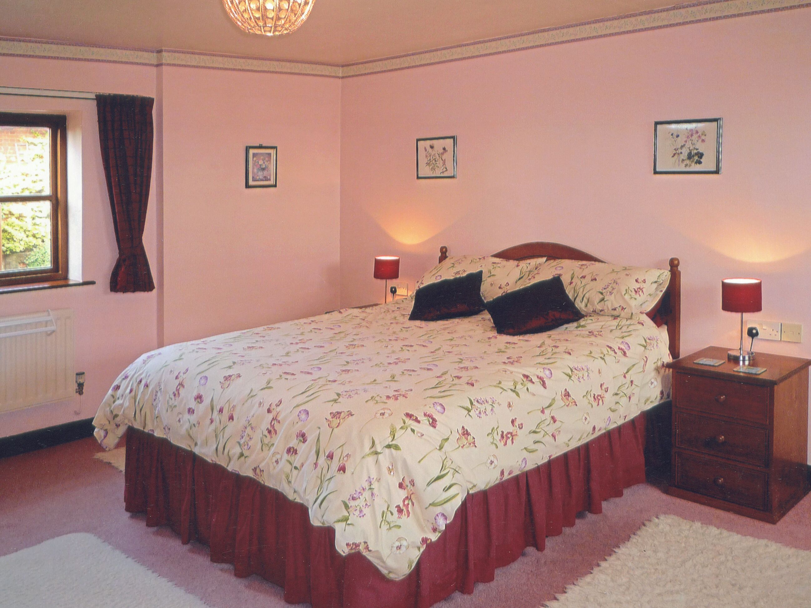 Una camera da letto con una coperta a fiori, due abat-jour, un comodino in legno e una finestra con tende.
