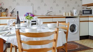 Een keuken met een eettafel voor twee personen, een wasmachine en een klok aan de muur.