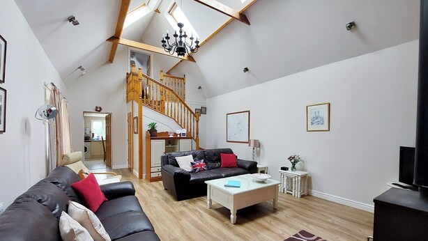 A spacious living room with a black leather sofa, a white coffee table, and a patterned rug. A wooden staircase leads to an upper level. - Peacock Barn - E5479 (Timberland, near Woodhall Spa)
