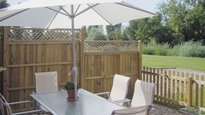 An outdoor patio with a table and chairs, a potted plant, and a wooden fence. - Peacock Barn - E5479 (Timberland, near Woodhall Spa)