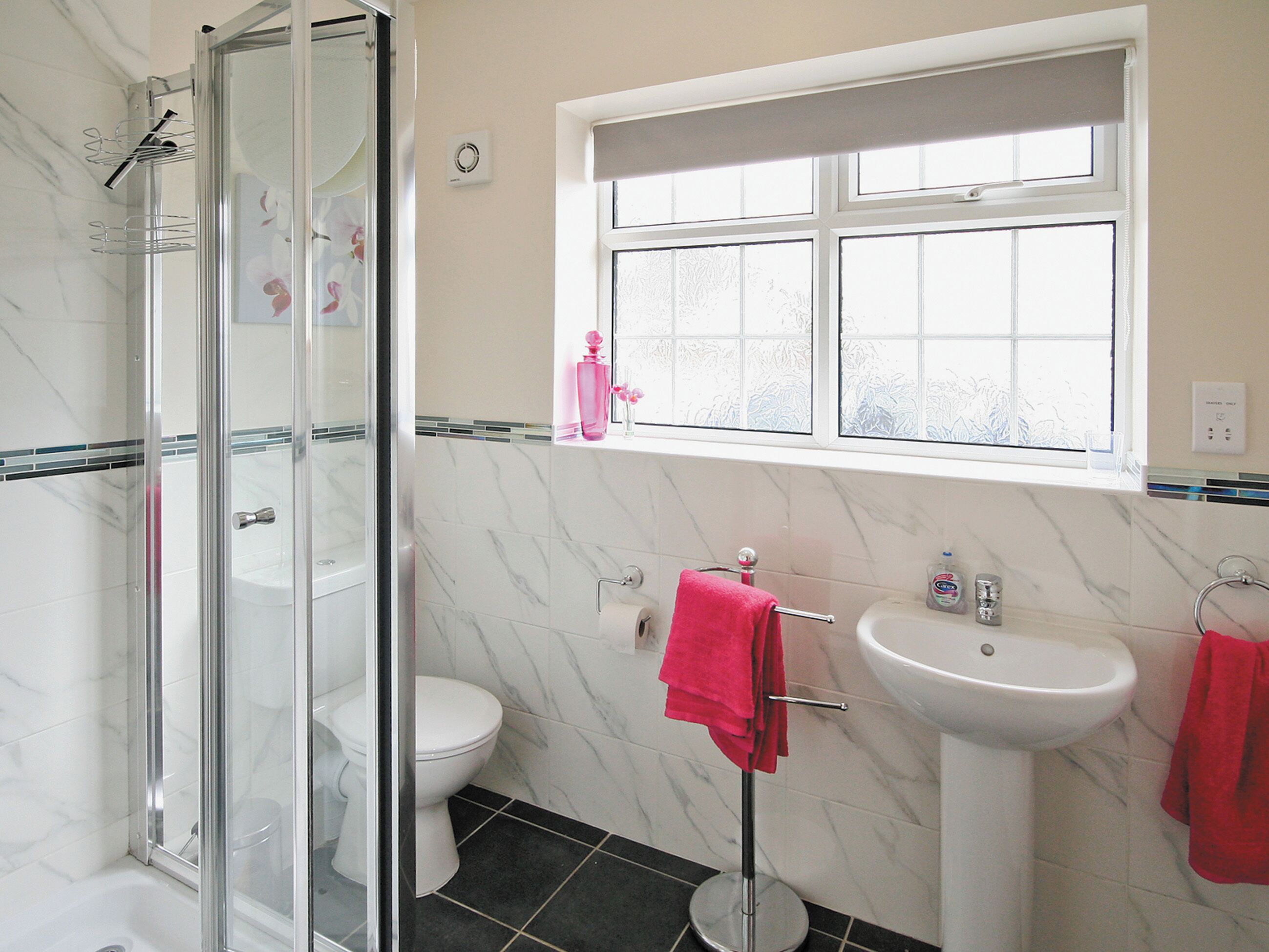 A bathroom with a glass shower enclosure, a toilet, a sink, and a window.
