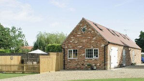 A brick building with a pitched roof, a wooden fence, and a gravel driveway. - Peacock Barn - E5479 (Timberland, near Woodhall Spa)