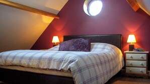 A bedroom with a sloped ceiling, a bed with plaid bedding, two bedside lamps, and a circular skylight. - Peacock Barn - E5479 (Timberland, near Woodhall Spa)