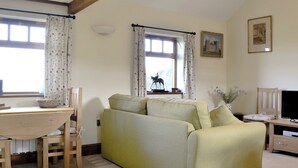 A living room with a sofa, a wooden table, a chair, a television, and a window with curtains.